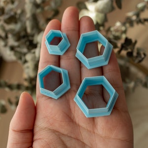 May include: Four blue plastic hexagon-shaped cookie cutters of different sizes.