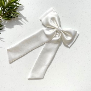 May include: A large white satin bow with long tails. The bow is tied in a classic style with the tails extending out to the sides.