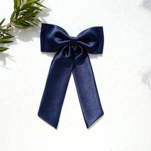 May include: A navy blue satin hair bow with long tails. The bow is tied in a classic knot and the tails are long and flowing.