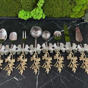 Puede incluir: Un juego de cubiertos de plata con mangos de mariposa dorados. El juego incluye una cuchara, un tenedor, un cuchillo y dos cucharones.