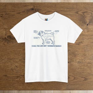 Puede incluir: Camiseta blanca con un diagrama esquemático azul de un pug, con etiquetas que señalan las partes del cuerpo. El texto "MODEL: PUG-LOV3 UNIT / SCHEMATIC DIAGRAM" está impreso debajo. La camiseta se muestra sobre una superficie de madera.