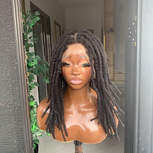 May include: A shoulder-length black wig featuring textured locs with a lace front base. The wig is displayed on a smooth, brown-toned mannequin head with defined facial features, including dark eyes, arched eyebrows, and light-colored lips.