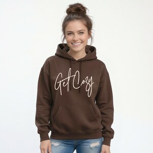 Woman wearing a brown Get Cozy hoodie with white script and jeans for a cozy fall outfit.