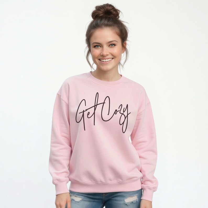 Woman wearing a light pink Get Cozy sweatshirt with black script and distressed jeans for a cozy fall outfit.