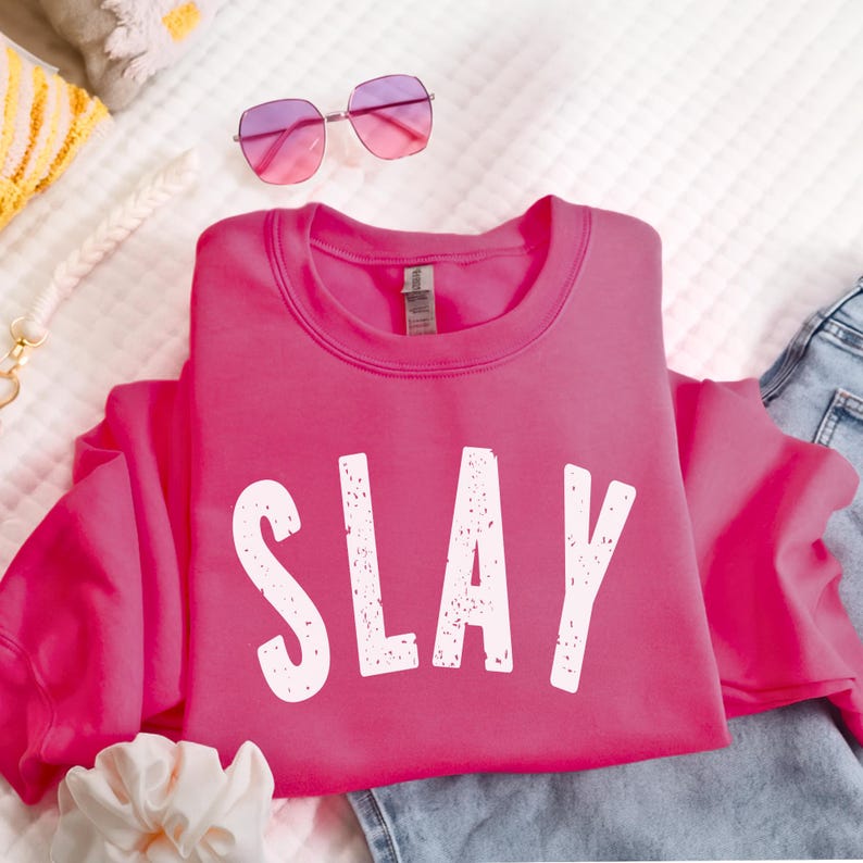 Dark pink SLAY crewneck sweatshirt with white bold distressed lettering, styled with casual accessories. Trendy graphic sweatshirt for teen girls, tweens, and women who love bold, confident fashion. Youth and adult sizes available.