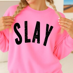 Bright pink sweatshirt with black SLAY graphic, cozy fleece crewneck for girls and teens, stylish youth fashion mockup, trendy bold lettering design.