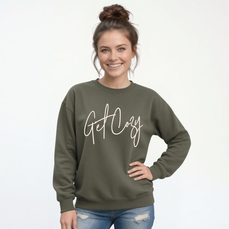 Woman wearing a military green Get Cozy sweatshirt with white script and distressed jeans for a cozy fall outfit.