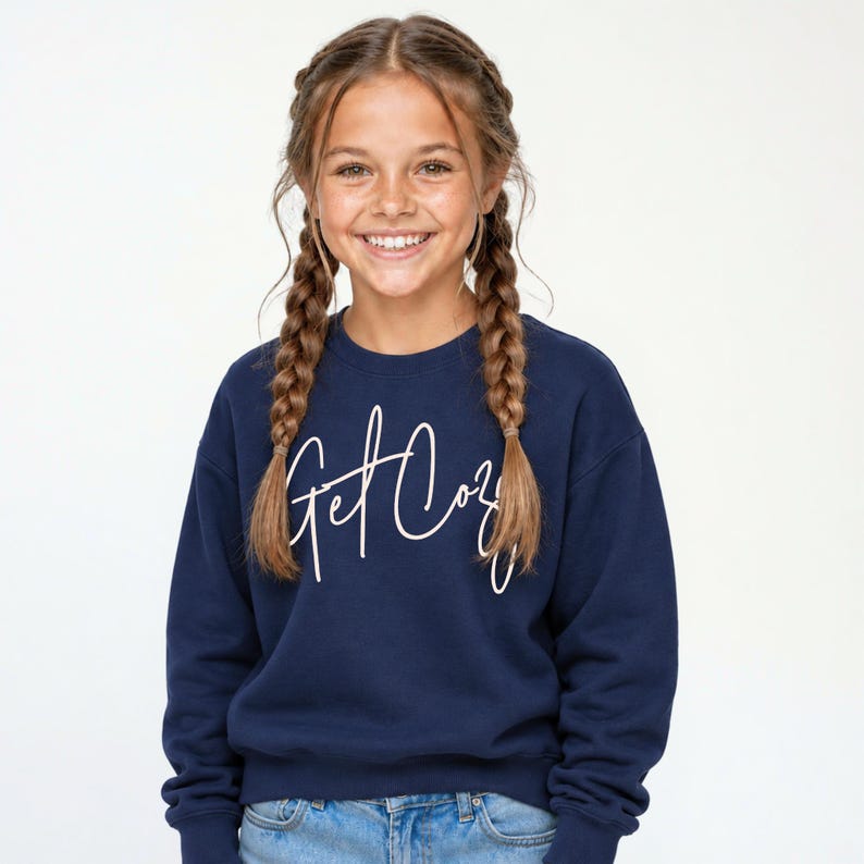 Girl wearing a navy Get Cozy youth sweatshirt with white script and light wash jeans.
