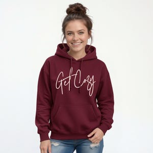Woman wearing a maroon Get Cozy hoodie with white script and jeans for a cozy fall outfit.