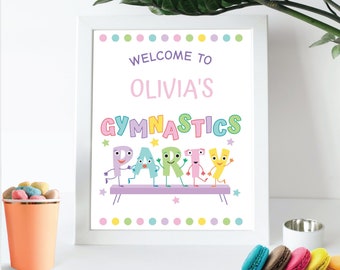 May include: A framed sign with the text "WELCOME TO OLIVIA'S GYMNASTICS PARTY" in colorful letters. The sign features cartoon characters and pastel polka dots. A peach-colored cup with candies and colorful macarons are in the foreground.