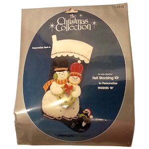 May include: A Christmas stocking kit featuring a snowman couple design. The kit includes felt pieces to personalize the stocking, which finishes at 18 inches. The packaging includes the text "The Christmas Collection" and "Mr. & Mrs. Snowman".