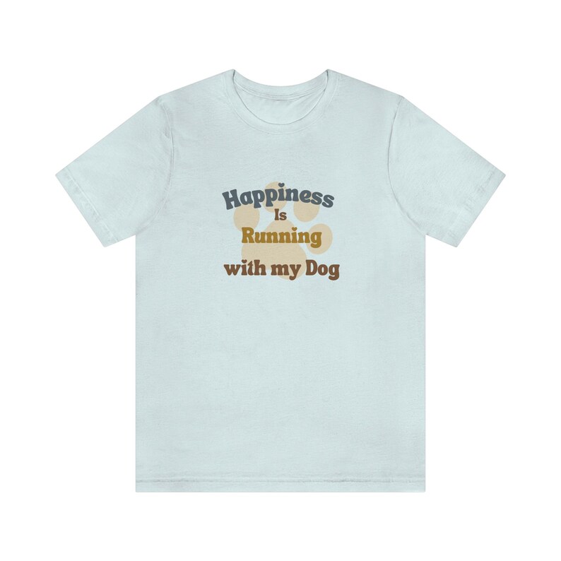 May include: A light blue t-shirt with the text 'Happiness is Running with my Dog' in dark blue and brown text. A paw print graphic is behind the text in a light brown color.