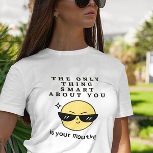 May include: White t-shirt with a yellow cartoon face wearing sunglasses and the text "THE ONLY THING SMART ABOUT YOU is your mouth!"
