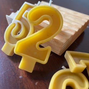 Puede incluir: Primer plano de velas amarillas de cera de abeja con números, incluyendo los números 5 y 2, con mechas blancas. Las velas están sobre una superficie de madera. Las velas son para una celebración de cumpleaños.