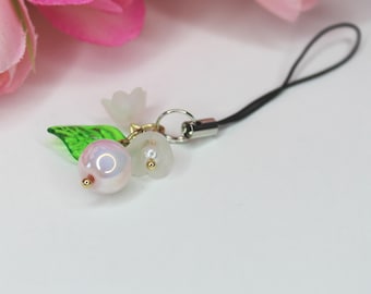May include: A white and green flower charm with a pearl bead and a black phone strap.