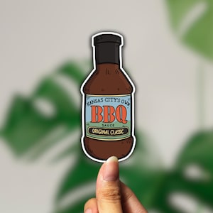 Peut inclure: Un autocollant repr&eacute;sentant une bouteille en verre marron de sauce barbecue avec une &eacute;tiquette bleue et blanche indiquant "Kansas City's Own BBQ Sauce Original Classic".