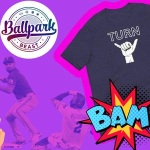 May include: A navy blue t-shirt with white text that says "TURN" and a white hand making a shaka sign. The t-shirt is on a pink background with a colorful graphic that says "BAM!" in a comic book style.