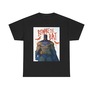 Peut inclure: Un t-shirt noir à manches courtes avec un imprimé central représentant un super-héros musclé en costume bleu et gris avec une ceinture utilitaire jaune. Au-dessus, le texte BEWARE THE BAT est écrit en rouge avec des icônes de chauve-souris.