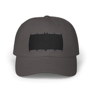 Puede incluir: Gorra de béisbol gris antracita con un emblema negro bordado en la parte delantera. El emblema tiene forma rectangular con un borde dentado. La gorra tiene una visera curva y una parte superior redondeada.