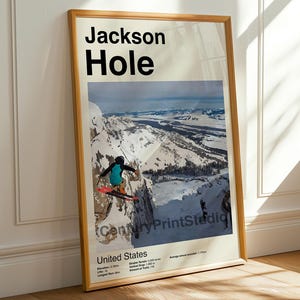 May include: Framed poster featuring a skier in mid-air over a snowy mountain landscape. The poster includes the text "Jackson Hole" in bold black letters, with additional text indicating the location as United States.