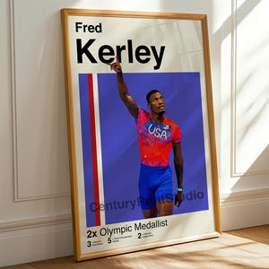 May include: Framed poster featuring Fred Kerley, a 2x Olympic medalist, in a red and blue athletic uniform. The poster includes the text "Fred Kerley" in large black letters and "USA" on the athlete's shirt. The poster is in a wooden frame.
