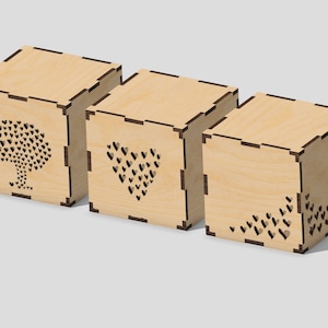 Puede incluir: Tres cajas de madera con intrincados diseños cortados con láser. Las cajas presentan un árbol, un corazón y un patrón de corazones.