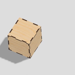 Puede incluir: Una pequeña caja de madera con un acabado marrón claro y un borde negro. La caja está hecha de madera y tiene un diseño simple y elegante.