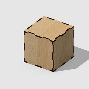 Pode incluir: Uma pequena caixa de madeira com acabamento marrom claro e uma borda preta. A caixa é quadrada e tem um design simples.