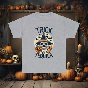 Peut inclure: T-shirt gris avec un crâne portant un chapeau de sorcière et tenant une bouteille de tequila. Le texte sur le t-shirt est "Trick or Tequila".