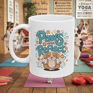 May include: White ceramic coffee mug featuring a colourful illustration of a dog meditating with the text "Paws and Reflect".