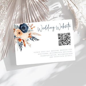 May include: A white card with a blue and orange floral design in the top left corner. The text "Wedding Website" is in blue script font. A QR code is in the center of the card. The text "PLEASE VISIT OUT WEDDING WEBSITE FOR ADDITIONAL INFORMATION INCLUDING TRANSPORTATION, ACCOMODATION AND RECEPTION DETAILS." is in gray text below the QR code.