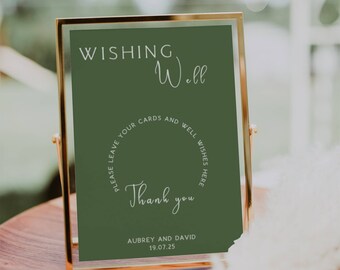 May include: A gold-framed sign with a green background and white text that reads "WISHING Well PLEASE LEAVE YOUR CARDS AND WELL WISHES HERE Thank you AUBREY AND DAVID 19.07.25".