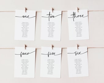 May include: Six white cards with black text hanging on a string with clothespins. Each card has a number from one to six written in cursive. The cards list names for a wedding seating chart.