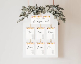 May include: A white board with a floral design and the text "find your seat" at the top. Six cards with floral designs and numbers one through six are hanging from the board with clothespins.