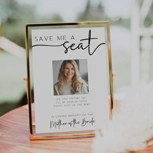 Puede incluir: Un cartel blanco con texto negro que dice "Save Me A Seat" con una foto de una mujer en el centro. El texto debajo de la foto dice "En este día especial estaré aquí en espíritu en cada paso del camino. En memoria cariñosa de la Madre de la Novia."