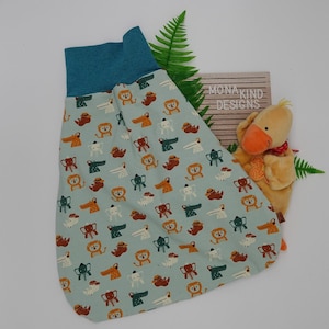 Könnte beinhalten: Ein hellblauer Schlafsack mit einem Muster aus verschiedenen Tieren, darunter Löwen, Elefanten, Krokodile und Vögel. Der Schlafsack hat einen türkisfarbenen Bund oben und ist aus weichem Stoff.