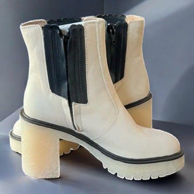May include: A pair of off-white ankle boots with a chunky platform heel and black zip detail. The boots have a pull-on style and a slightly pointed toe.