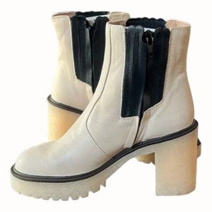 May include: White leather ankle boots with a black leather panel and zip detail. The boots have a chunky platform heel and a rounded toe.