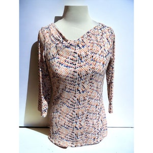 May include: A long-sleeved, cream-colored top with a cowl neck and an abstract print in shades of orange, blue, and black.