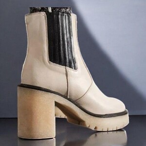 May include: A pair of cream-coloured ankle boots with a chunky heel and a black elastic panel at the back. The boots have a textured sole and a slightly pointed toe.