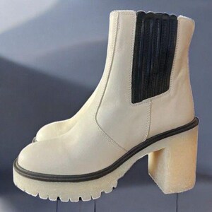 May include: White leather ankle boots with a black elastic panel on the back. The boots have a chunky heel and a platform sole.