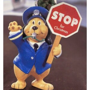 May include: A brown and yellow dog wearing a blue police officer uniform and a whistle around its neck. The dog is holding a red stop sign that says "STOP for Christmas".