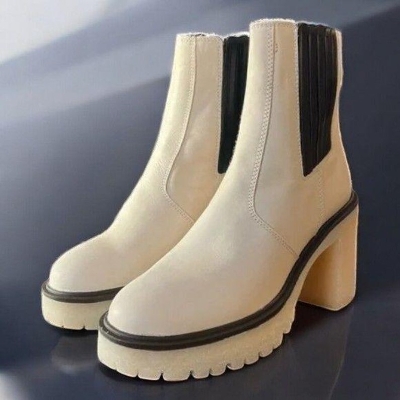 May include: A pair of off-white ankle boots with black elastic panels and a chunky heel. The boots have a platform sole and a rubber outsole.