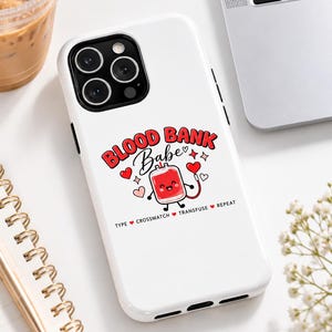 Puede incluir: Una funda de smartphone blanca con una ilustración de dibujos animados de una bolsa de sangre sonriente, el texto "BLOOD BANK Babe" y "TYPE CROSSMATCH TRANSFUSE REPEAT" en rojo y negro, rodeado de corazones rojos y estrellas.