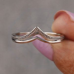 Puede incluir: Un anillo de plata con un diseño en forma de V. El anillo está adornado con pequeñas cuentas espaciadas uniformemente a lo largo de los bordes.