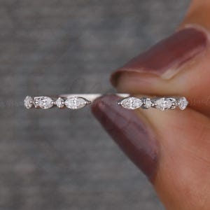 Puede incluir: Un delicado anillo de plata con gemas alternas en forma de marquesa y redondas. El anillo se sostiene sobre un fondo gris, mostrando el intrincado diseño y el brillo de las piedras. Una fina pieza de joyería.