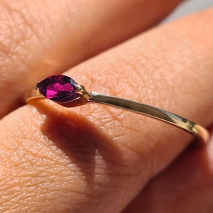 Könnte beinhalten: Ein goldener Ring mit einem einzigen, tiefvioletten Edelstein, der in der Mitte sitzt. Der Ring befindet sich an einem Finger.