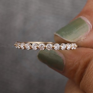Könnte beinhalten: Ein Ewigkeitsring aus Roségold mit einer durchgehenden Reihe kleiner, runder, klarer und facettierter Steine in einer gemeinsamen Krappenfassung. Der Ring hat eine dünne, polierte Metallschiene, die die Steine in einer geraden Linie hält.