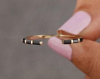 May include: A gold ring with black rectangular stones set in the band. The ring is open and is being held by a hand.