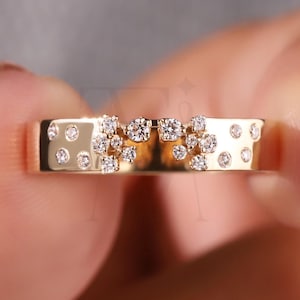 以下が含まれることがあります： 平らなバンドの金色のリングで、小さな輝くダイヤモンドで飾られています。 リングは、ダイヤモンドのクラスターと個々の石を特徴とし、繊細で人目を引くデザインを作り出しています。 リングは指の間に挟まれています。